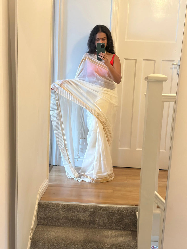 Elegant white pure mul cotton saree with gold zari border and tassels. Lightweight drape for festive and casual wear. LaiLai Sarees