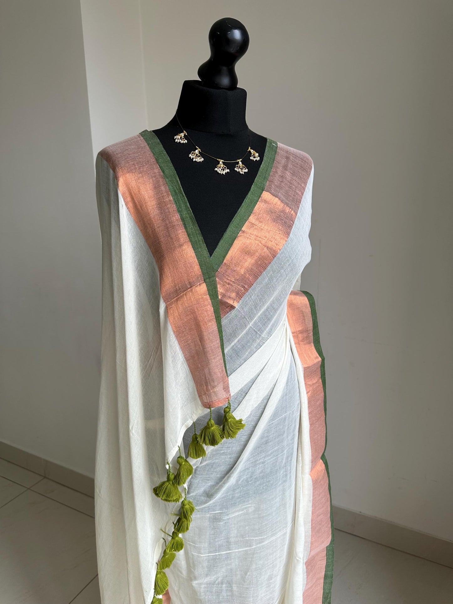 Elegant white mul cotton saree with copper zari border and green trim, lightweight handloom drape for festive and casual wear. Onam saree
