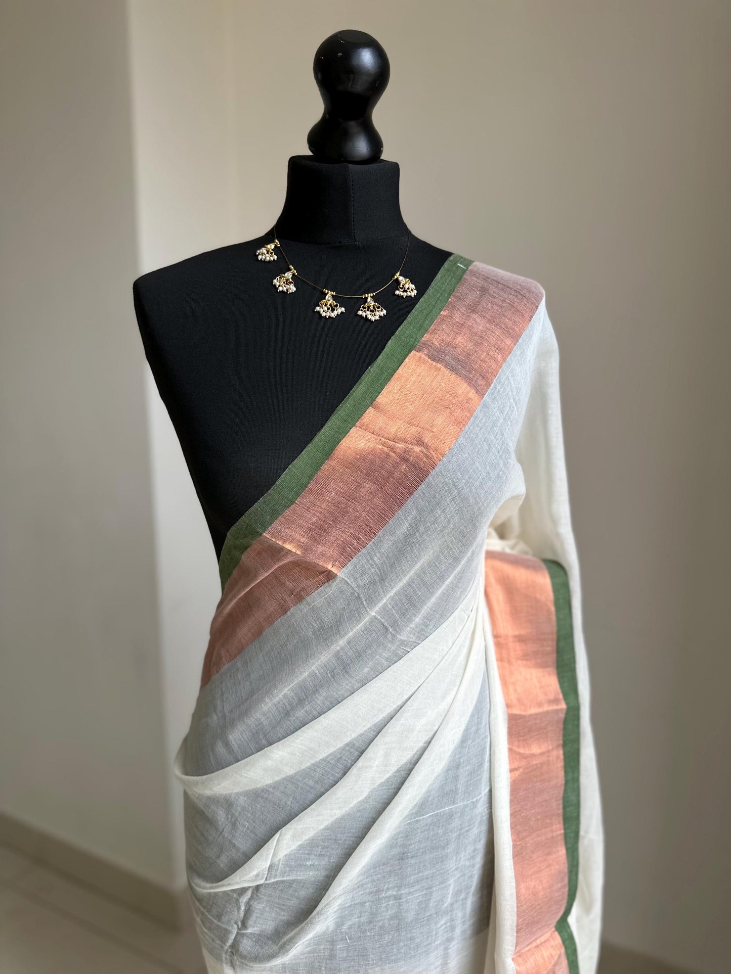 Elegant white mul cotton saree with copper zari border and green trim, lightweight handloom drape for festive and casual wear. Onam saree